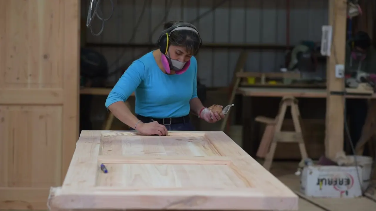 Operaria revisando un paño de puerta de madera en el taller